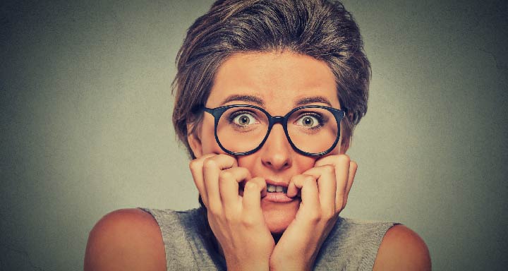 woman with short hair and glasses clutching her face looking scared