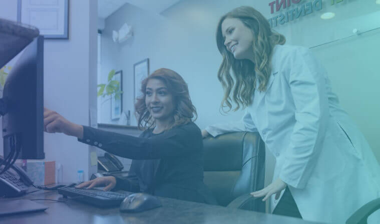 woman sitting at desk pointing to a screen and smiling as a doctor leans over her shoulder looking at the screen and smiling