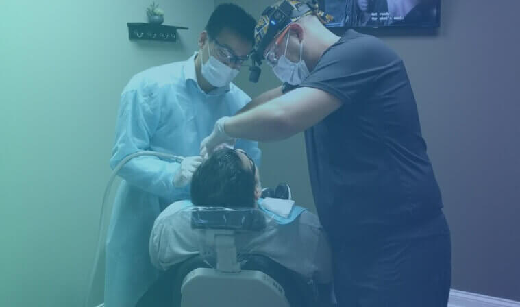 Young man sits in dentist's chair, while receiving a dental exam by a dentist and hygienist