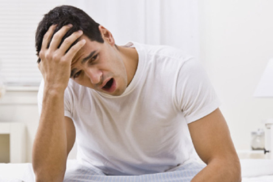 man holding his head sitting on the edge of the bed after a night of sleep apnea