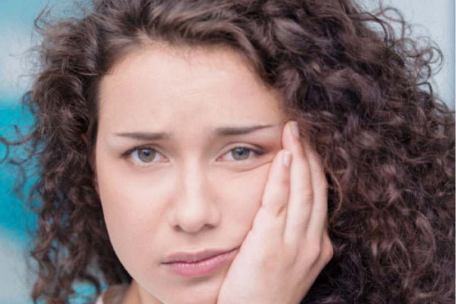 young woman holds her jaw in pain from wisdom teeth coming in