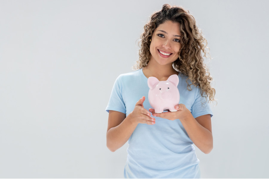 young woman smiles and holds a piggybank happy to have affordable dental care