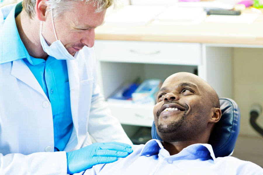 man sits in the dentist chair and confers with the dentist after a gum exam