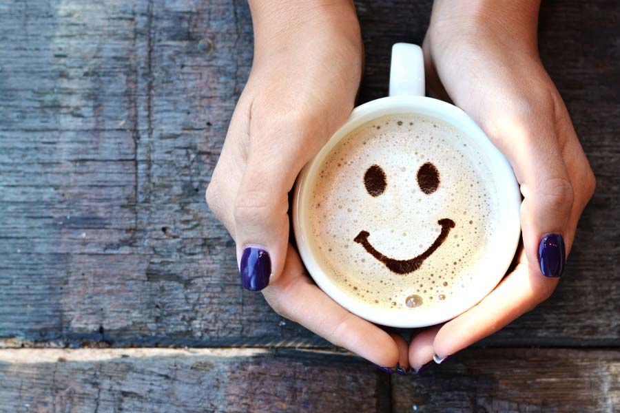 hands hold a cup of coffee with a happy face in the froth